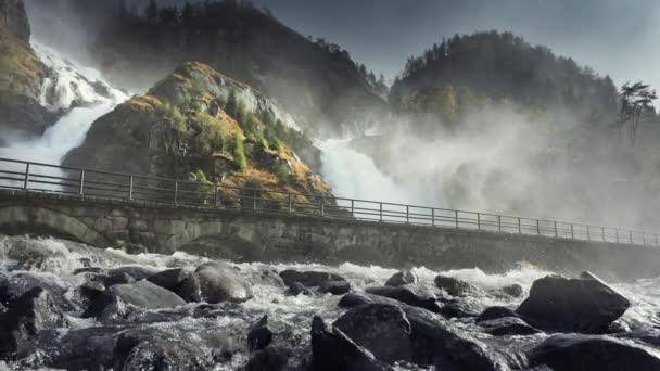 レイジングLatefossen滝 雨によって供給される水の強力な急流は 森林に覆われた崖から突入し 浅い山の川に合流します 水のほこりが道路に落ちる スローモーション パン右 — ストック動画