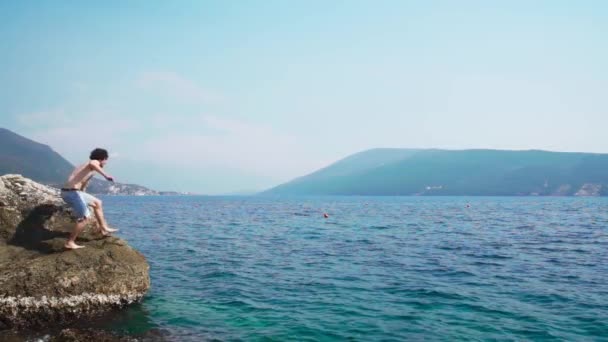 若い白人男性が岩から海に飛び込んだ スローモーションビュー — ストック動画