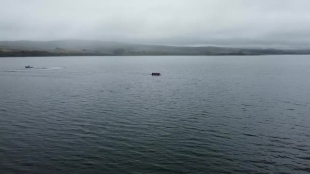 青い海の真ん中を航行する小型ボートでラフティングする人々の空中ショット 見事な霧の山の背景 カリフォルニア州 — ストック動画