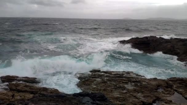 風が強く曇りの日の海で波が岩や暗い嵐の雲に打ち寄せる スローモーション 右に曲がることでショットビュー ポンテベドラ ガリシア スペイン — ストック動画