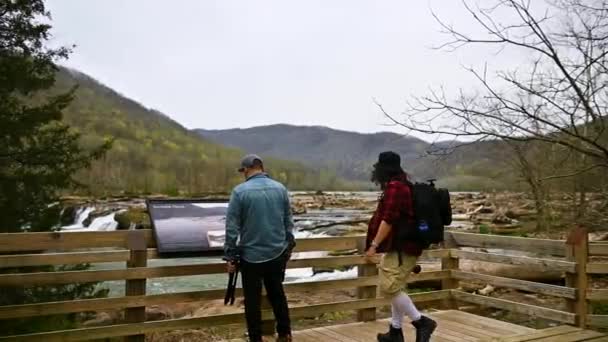 二人の男が散歩に行き 木製の橋の前に立つ 一つは山の美しさを楽しむこと もう一つは木製の橋のガイドに瞑想している — ストック動画