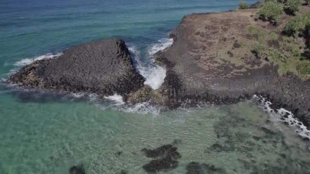 波が海でサーファーと六角形の火山岩の形成に飛び出すことが明らかになりました オーストラリアのニューサウスウェールズ州のタスマン海の指頭コーズウェイ 空中プルバック — ストック動画