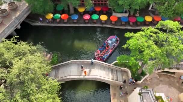 驳船航行圣安东尼奥河步行场景 人们乘坐的小船经过五彩斑斓的餐厅雨伞和行人脚桥 空中景观 — 图库视频影像