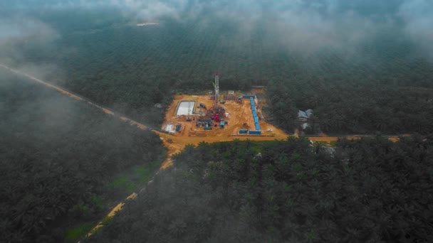 夕暮れ時にパーム油の木に囲まれたジャングルの中での石油探査と搾取のための陸上掘削と作業用リグ構造物とリグ機器のシネマティックドローンショット — ストック動画