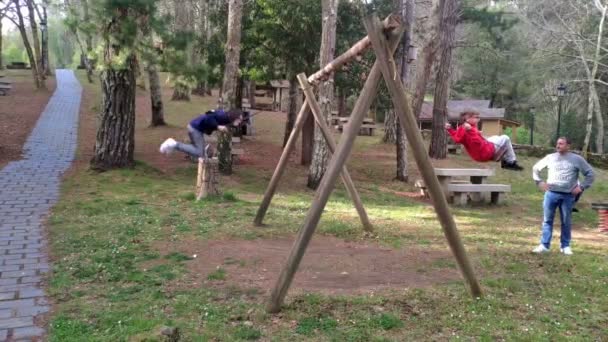 Children Playing Swings Nature Park Trees Father Taking Care Them — Vídeo de stock