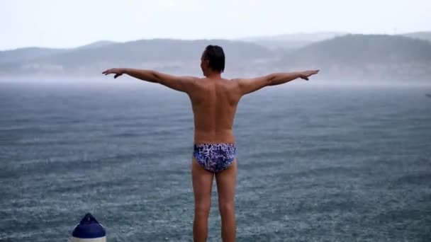 海水浴場で腕を伸ばして立つ水着姿の男の後ろ姿 フルショット — ストック動画