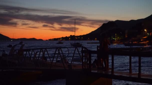 シルエットの女性は湖に浮かぶボートで日没時に桟橋を歩く — ストック動画