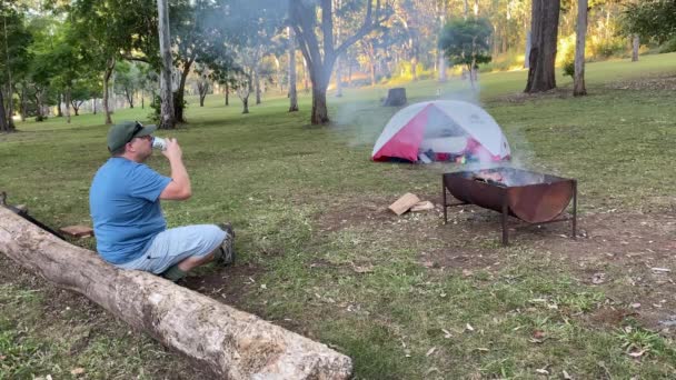 Man Zittend Een Stam Bier Drinkend Bij Een Kampvuur — Stockvideo