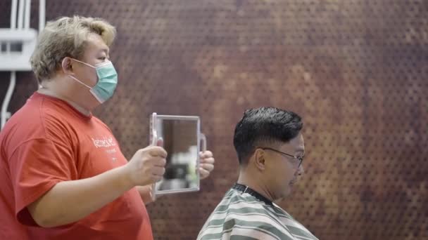 在专业美发厅 理发师佩戴口罩 向满意的顾客展示带有镜子的短发 — 图库视频影像
