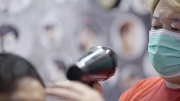一位理发师正在用烘干机烘干一位顾客的头发 他戴着外科口罩 — 图库视频影像