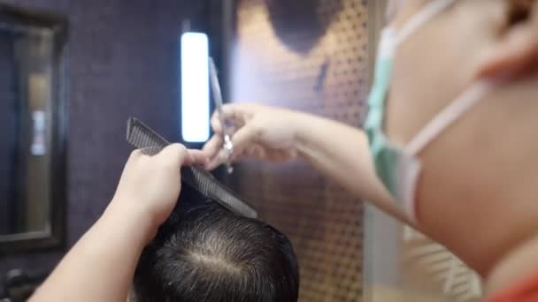 一个带着剪刀和黑色梳子 戴着面具的年轻理发师在顾客头上剪头发的商业视频 — 图库视频影像