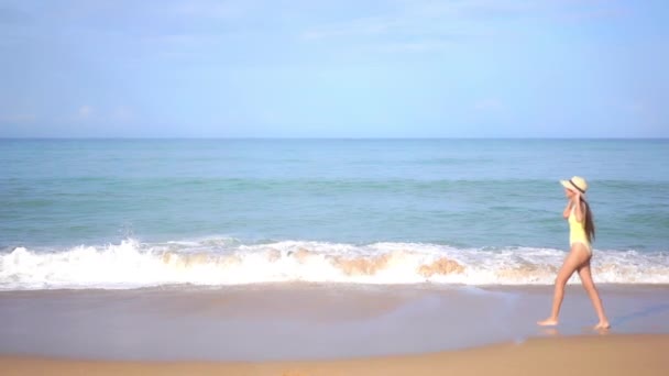 身穿黄色泳衣的亚洲成年女子在沙滩上走在海边 — 图库视频影像