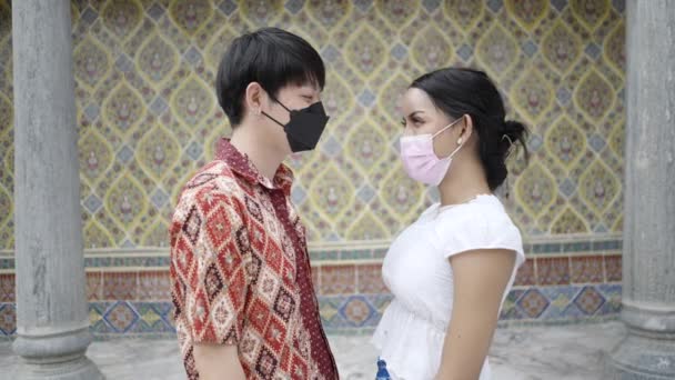 日本人男性とトランスジェンダーのタイ人カップルがお互いの前に立って保護マスクを着用し 美しい目を見ます — ストック動画