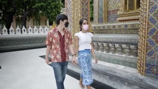 トランスジェンダーアジアのカップルは ワット ラチャボフィット サティマハシマーラム ラチャワウィハン仏教寺院を訪れる呼吸マスクで手をつないで散歩 — ストック動画