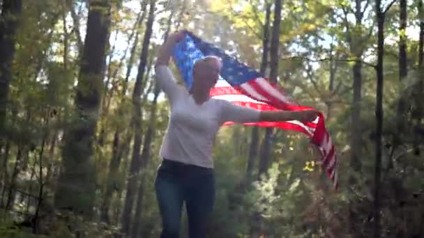 Mujer Rubia Bonita Retroiluminada Caminando Por Bosque Sosteniendo Una Bandera — Vídeos de Stock