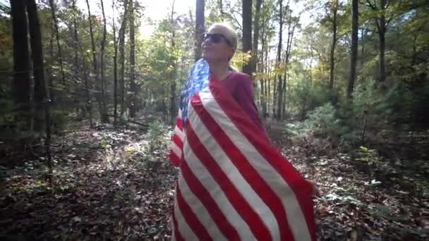 Красивая Блондинка Заворачивающая Себя Флаг Пока Камера Вращается Вокруг Лесу — стоковое видео