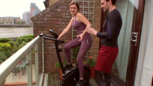 Young Woman Riding Exercise Bicycle Balcony Overlooking River Boyfriend — Video