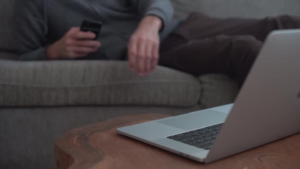 Man Lying Sofa Home Uses Mobile Phone Types Laptop — Stock video