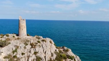 İnsansız hava aracı bir sahil gözetleme kulesinin üzerinden uçuyor, mavi deniz uçurumunun üzerinde yüzüncü yıl kulesi ve güzel bir hava manzarası olan kayalar.
