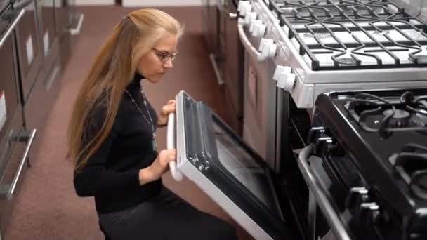 Pretty Mature Blonde Woman Squatting Looking Stove Kitchen Appliance Store — 图库视频影像