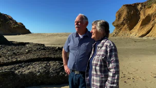 Senior Couple Beach Laughing Pointing Cliffs Background 24K Slow Motion — Stockvideo