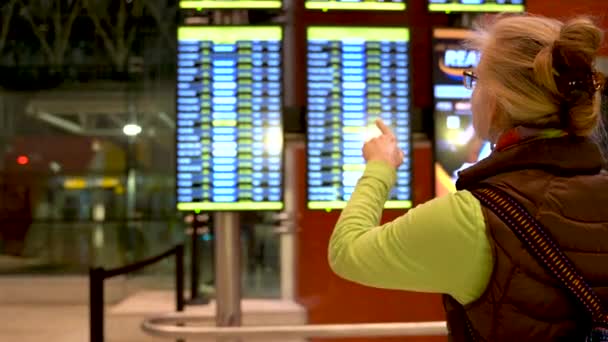 Жінка Блондинка Вказує Показ Інформації Аеропорту Тримаючи Свій Смартфон — стокове відео