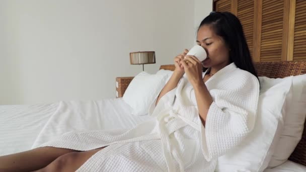 Young Woman Wearing White Dressing Gown Laying Hotel Bed Drinking — Videoclip de stoc