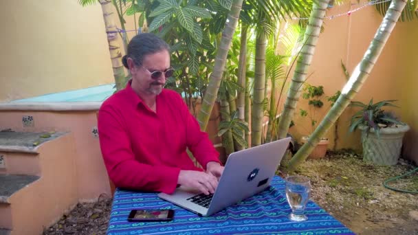 Mature Man Smiles Sits Table Garden Working Computer Wearing Guayabera — 图库视频影像