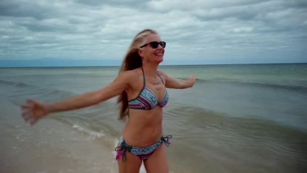 Front Shot Playful Blonde Mature Woman Sunglasses Bikini Running Shore — Stockvideo