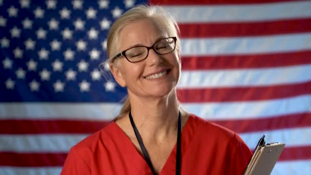 Retrato Una Enfermera Asintiendo Con Cabeza Sonriendo Contra Una Bandera — Vídeo de stock