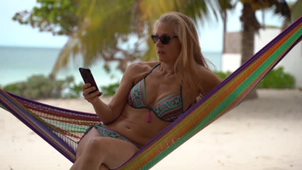 Pretty Mature Woman Sunglasses Bikini Hammock Texting Smartphone Shaking Her — Video Stock