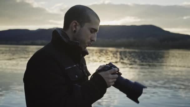 Young Caucasian Man Looking Adjusts Handheld Camera Standing Calm Lake — Stock video