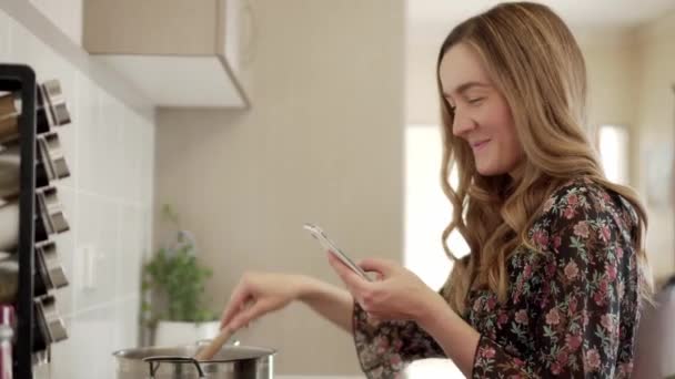 Smiling Young Woman Uses Smart Phone Kitchen While Cooking Stove — Stock Video