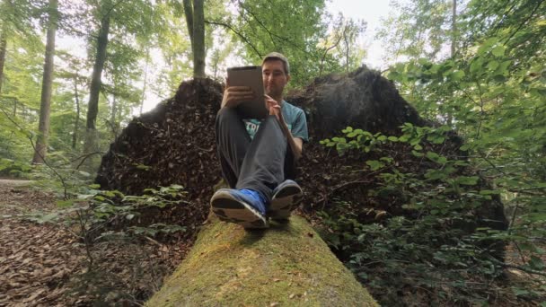 Man Swiping His Tablet Computer While Sitting Tree Trunk Sunny — Stok Video