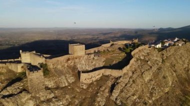 A drone circles Marvao Castle while a flock follows it during sunset.