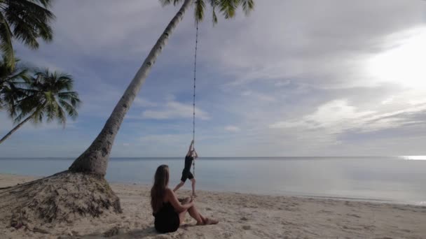 Young Caucasian Man Rope Swinging Palm Tree Beach Young Woman — Vídeo de stock