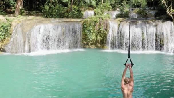 Young Caucasian Man Blond Hair Rope Swinging Turquoise Natural Pool — Stockvideo