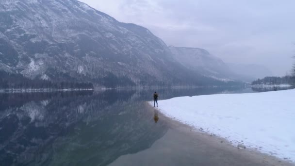 Man Walks Alone Snowy Bohinj Lake Reflecting Mountains Distance Aerial — Vídeo de Stock