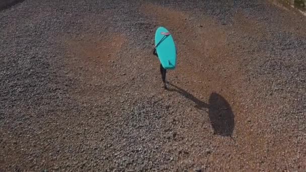 Young Man Walking Out Sea Pebble Beach Blue Paddle Board — Stockvideo