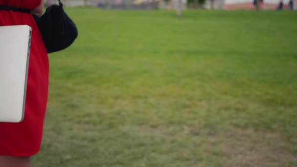 Follow Detail Shot Woman Red Dress Holding Laptop Walking Park — Vídeo de Stock