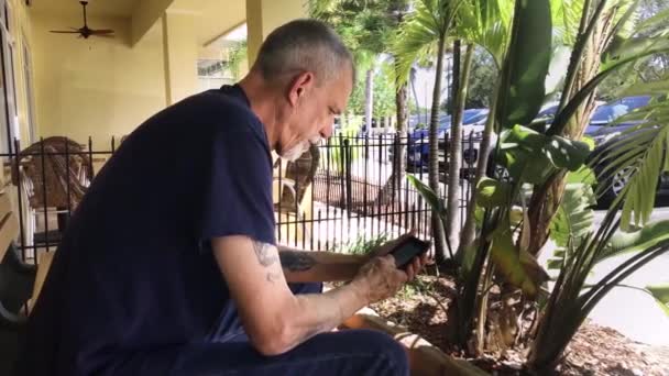 Elderly Man Sitting Using His Mobile Device Tropical Setting — Vídeo de stock