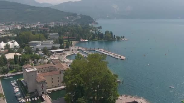 前景に古い城とリヴァ ガルダの港の美しいドローンショットと背景に湖の庭とイタリアのアルプス — ストック動画