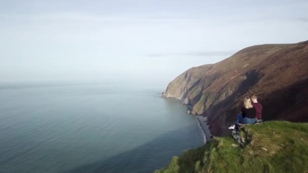Couple Sat Cliff Edge Overlooking Ocean Drone Shot Dolly Forward — Vídeo de Stock