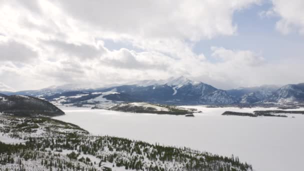 Aerial Moving Backward Icy Frozen Lake Surrounded Snow Green Pine — Stockvideo