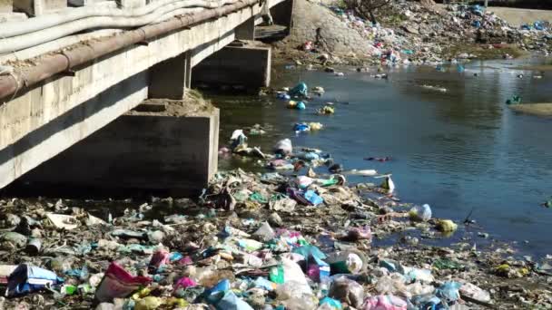 コンクリート橋の近くのプラスチックやその他のゴミで満たされた地元の川 静的なビュー — ストック動画