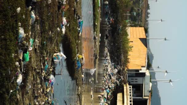 ベトナムの川の近くの前景にプラスチックごみの山が散在している間 風車は背景で働いています — ストック動画