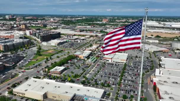 アメリカの国旗は誇らしげにアメリカの都市を飛び越える 小売ショッピングモール オフィスビル 家庭や家 航空軌道 — ストック動画