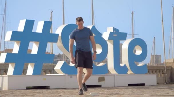 Young Athletic Caucasian Man Turning His Music Speaker Squats Front — Stockvideo