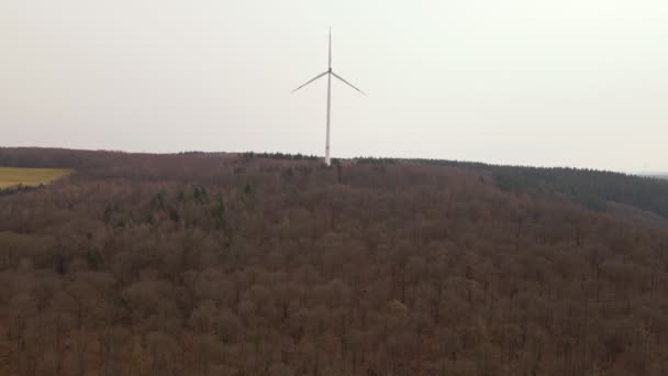 Spinning Wind Turbine Top Ridge Numerous Leafless Deciduous Trees Aerial — Stockvideo