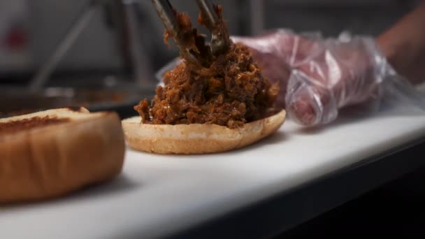 Cook Uses Tongs Place Chopped Beef Toasted Bun Barbecue Sandwich — Stockvideo